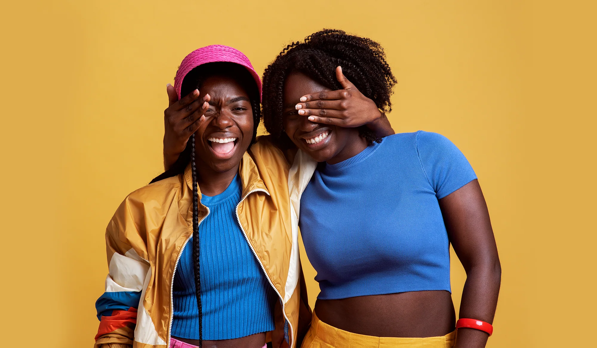 Two friends laughing together against a warm yellow backdrop