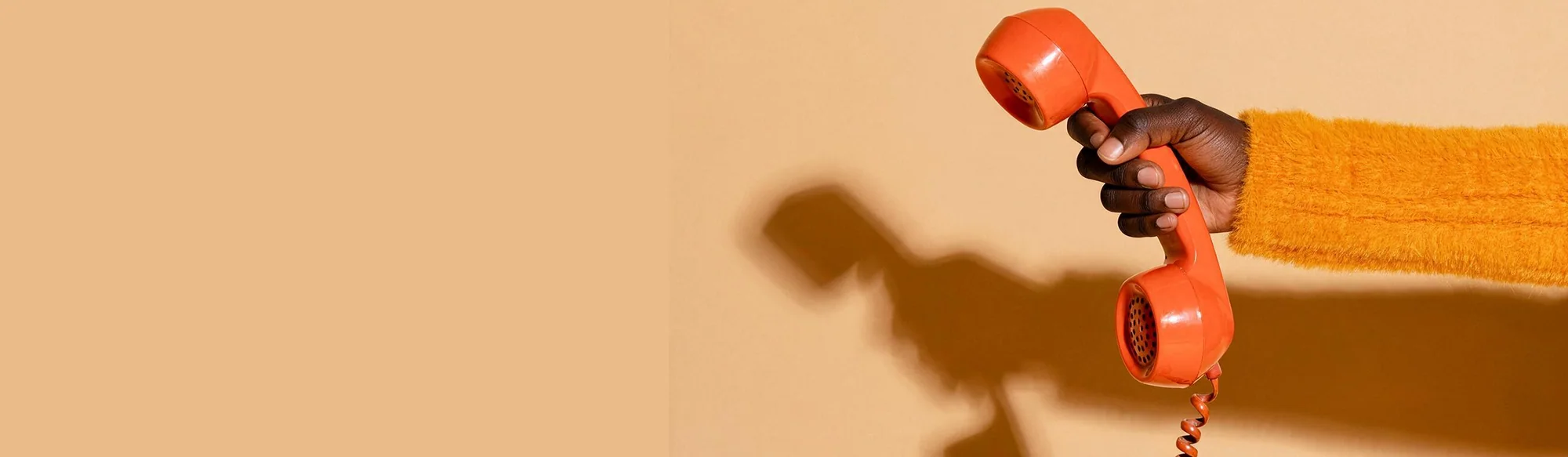 A hand holding a bright orange telephone receiver